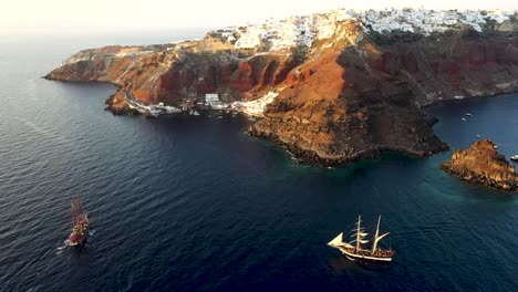 Aerial-drone-view-video-of-beautiful-sail-boats-cruising-in-the-deep-blue-Aegean-sea-during-sunset,-Santorini,-Greece