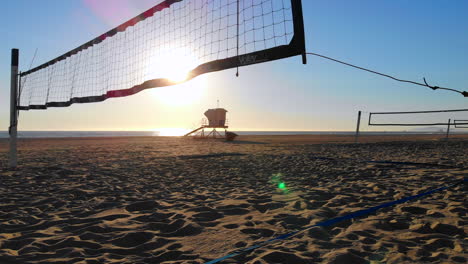 Low-fly-to-empty-volleyball-nets-with-beautiful-sunset-and-lifeguard-tower-in-distance,-aerial-4k-drone-in-Huntington-Beach,-CA