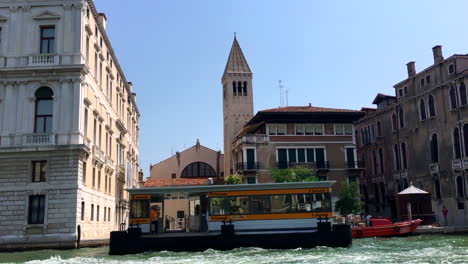 Venice,-Italy-water-taxi-station-and-church-bell-tower-shot-from-boat-on-Grand-Canal,-HD