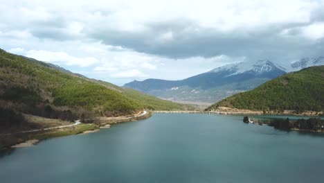 Drone-Disparó-Sobre-Un-Bosque-Y-Un-Lago-Con-Un-Pico-De-Montaña-Nevado-En-El-Fondo,-Grecia