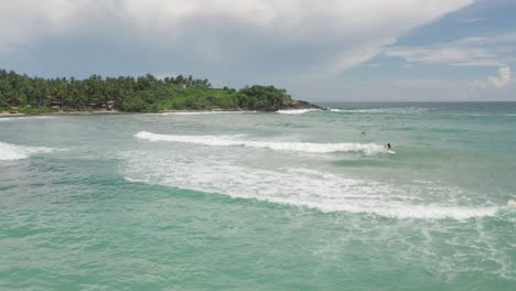 Surfers-riding-tranquil-waves-at-Hiriketiya-Beach-in-tropical-Sri-Lanka