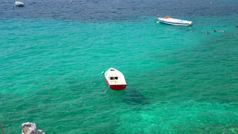 White-and-red-wood-boat-floating-in-turquoise-sea-water,-Peloponnese