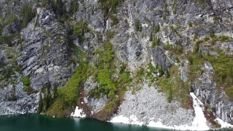 Drone-footage-of-mountain-waterfall-and-Colchuck-Lake-near-The-Enchantments-in-Washington's-Cascade-Mountain-Range---Moss-and-Tress-grow-on-the-cliffside