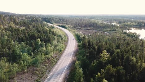 Forward-drone-shot-over-motorcyclist-riding-a-road-inside-a-forest-in-north-Finland,-Europe,-above-the-arctic-circle