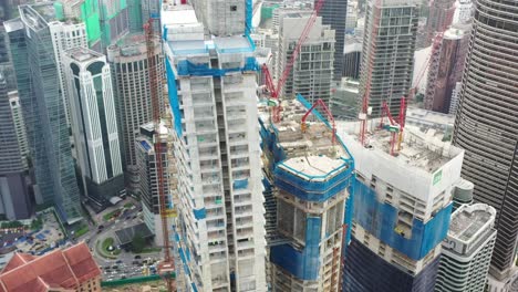 Fly-around-imperial-lexis-high-rise-building-under-construction-surrounded-by-high-density-downtown-cityscape,-urban-development-in-kuala-lumpur,-malaysia,-asia