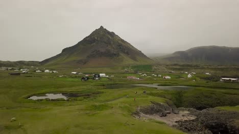 Aerial-Footage-of-Moutain-Over-Wooden-Houses-and-Lake-During-Cloudy-Summer-In-Hellnar,-Snaefellsness-Peninsula,-Iceland