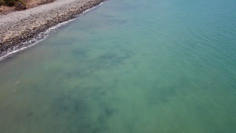 Drone-flying-low-on-water-slow-pan-up-over-blue-tropical-beach-water