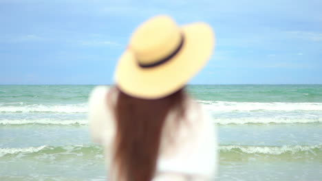 Close-up-of-a-woman-with-her-back-to-the-camera-walking-into-the-frame-toward-the-incoming-tide