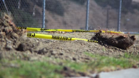 An-empty-desolate-park-enclosed-by-a-chain-link-fence-where-the-wind-blows-caution-tape-attached-to-a-dirt-rock