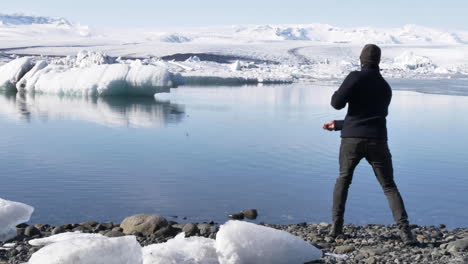 Junger-Männlicher-Reisender,-Der-In-Zeitlupe-Steine-In-Der-Wunderschönen-Gletscherlagune-Islands-überspringt