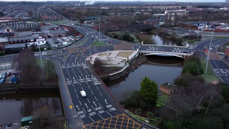 Aerial-early-morning-city-street-traffic-commuting-intersection-lanes-crossing-curved-river-descending-tilt-up