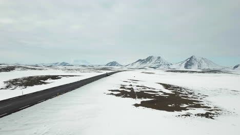 Disparo-De-Dron-De-Un-Automóvil-Conduciendo-A-Través-De-Un-Paisaje-Frío-Y-Hermoso-En-Una-Carretera-Vacía-En-Islandia