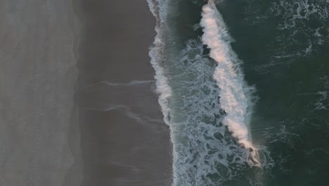 White-Foamy-Waves-Rolling-Up-To-The-Sandy-Shore---Aerial-Pan-Up,-Slow-Motion