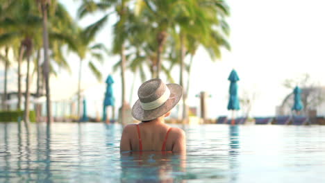 Woman-with-large-hat-in-pool-resort-expresses-happiness-concept-by-raising-arms