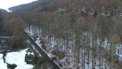 Snowy-Welsh-woodland-Moel-Famau-winter-landscape-aerial-descending-following-rural-road