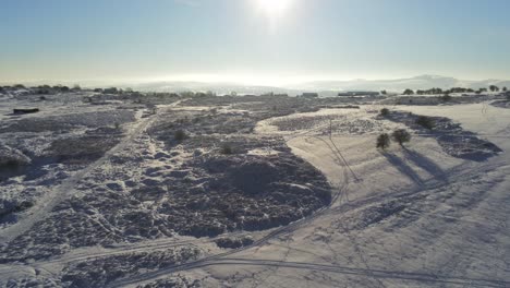 Snow-covered-rural-winter-countryside-track-footprint-shadows-terrain-aerial-slow-pull-back-view