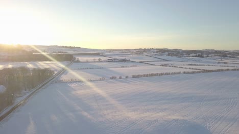 Winter-landscape-with-a-house-and-fields-covered-with-white-snow-till-the-horizon-on-a-bright-cold-day-in-Scotland-during-golden-hour-while-the-sun-is-on-top-of-the-hill