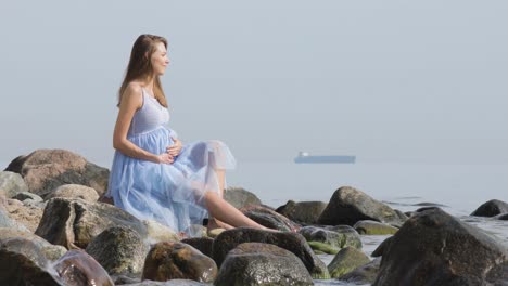 A-beautiful-young-pregnant-woman-sits-on-the-rocks-by-the-sea