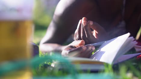 Niña-Africana-Escribiendo-En-Un-Cuaderno-Mientras-Se-Acuesta-En-El-Parque