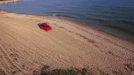 Aerial-View-car-driving-on-the-beach-in-greece-surrounded-by-blue-water