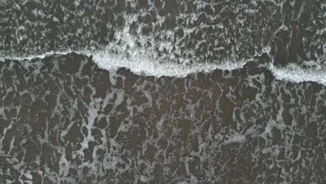 Aerial-shot-of-waves-crashing-into-sandy-beach-of-Ustka-in-winter