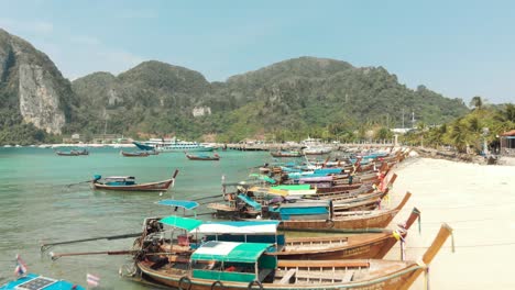 Group-of-Long-tail-boats-moored-along-the-shore-in-Tonsai-Bay,-Ko-Phi-Phi-Don-Island-Paradise-in-Thailand---Aerial-Low-Fly-over-shot