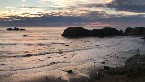 Panorama-of-Bandon-Beach-in-Oregon-at-sunset,-including-Face-Rock,-Elephant-head,-Cat-and-Kittens-rock-formations-and-people-enjoying-a-walk-on-the-beach