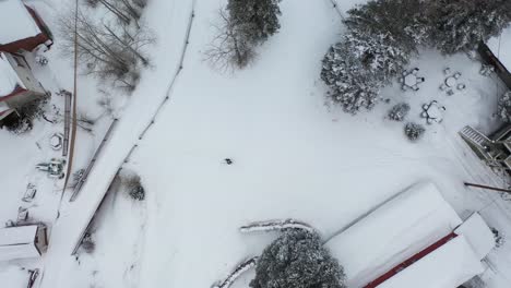 Birdseye-Aerial-View,-Lonely-Person-in-Snowshoes-Walking-on-Snow-Between-Houses