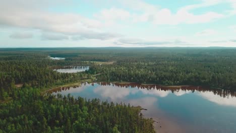 Forward-panning-drone-shot-over-forests-and-lakes-with-clouds-reflected-on-them-in-north-Finland