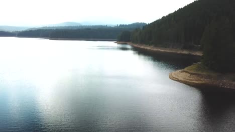 Forward-drone-shot-slightly-over-a-lake-gradually-elevating-with-a-forest-in-the-background