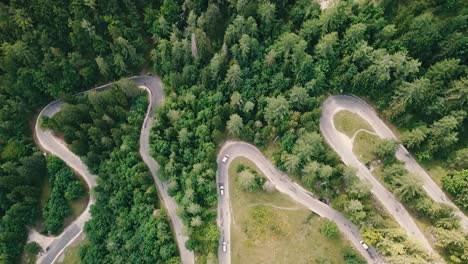 Bird's-eye-view-with-an-elevating-movement-of-a-winding-road-inside-a-forest-and-cars-passing-by