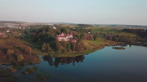 Elevating-pan-drone-shot-of-a-castle-next-to-a-lake-that-reflects-it