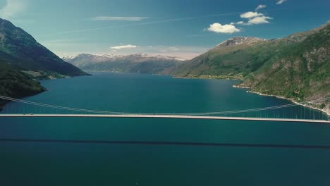 Crane-up-and-tilt-down-drone-shot-of-a-suspension-bridge-over-a-fjord-on-a-sunny-day