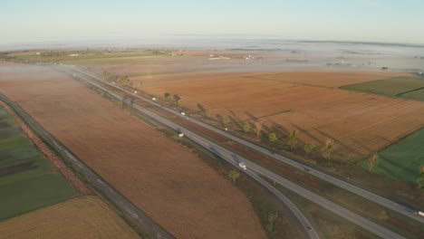 Niebla-Matutina-Sobre-El-Paisaje-Rural-Y-La-Carretera-Con-Automóviles-Y-Camiones-Conduciendo-Por-La-Carretera