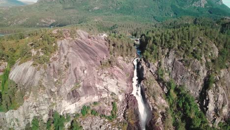 A-large-waterfall-in-Norway-and-a-green-forest-in-the-background,-dolly-drone-shot-in-4K