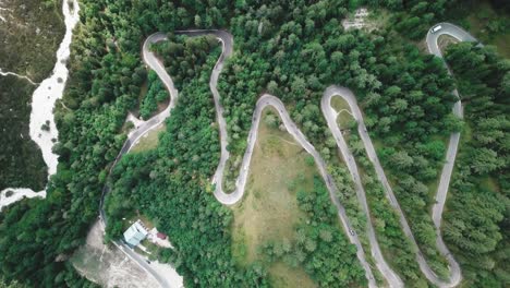 Bird's-eye-view-crane-down-movement-of-a-winding-road-inside-a-forest-and-cars-passing-by