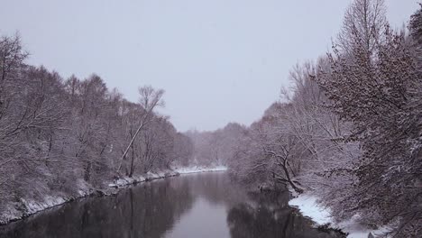 Gentle-snowfall-over-the-calm-river-source-in-the-middle-of-the-forest-in-northern-Europe---a-panorama-shot