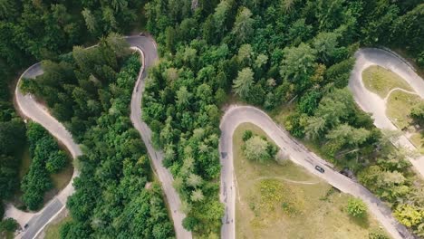 Bird's-eye-view-with-a-sideways-elevating-movement-of-a-winding-road-inside-a-forest-and-cars-passing-by