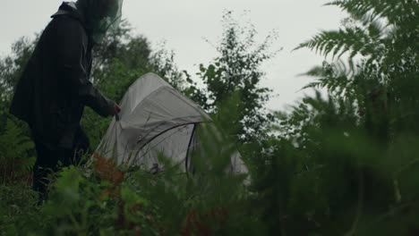 Empacando-Una-Carpa-En-Un-Exuberante-Bosque-Verde-Bajo-La-Lluvia-Usando-Un-Sombrero-De-Mosquito