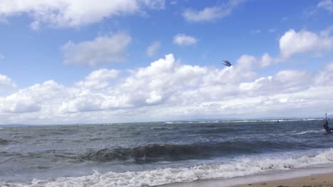 A-kite-surfer-moving-past-at-speed,-close-to-the-shoreline,-changing-direction-and-coming-back-|-Windy-summer-day,-Portobello-beach,-Edinburgh-|-Shot-in-HD-at-cinematic-24-fps