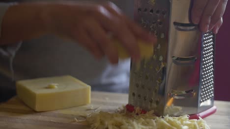 Woman's-hand-grating-cheese-onto-a-wooden-chopping-board