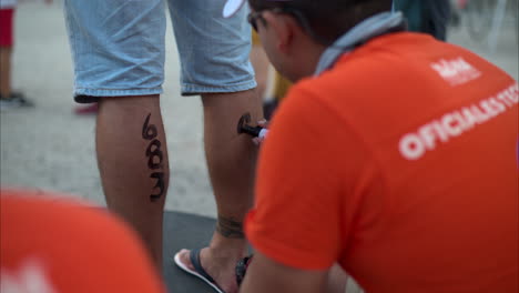 Triathlon-event-marshall-tagging-writing-the-athletes-number-on-the-legs-with-a-black-marker-before-the-competition