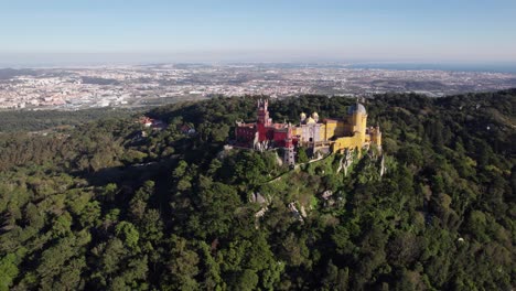 Cinematic-drone-shot-flying-away-and-revealing-the-vast-landscape-of-historic-Pena-Palace-castle-standing-a-top-of-a-hill-in-Sintra-mountains-above-town-of-Sintra,-Lisbon,-Portugal