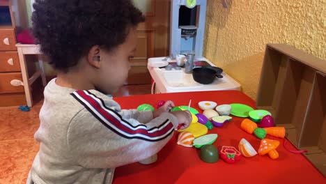 Sweet-two-year-old-black-baby,-mix-raced,-chopping-vegetables-to-cook-in-his-toy-kitchen-at-home