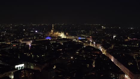 Milan-cityscape-and-glowing-Cathedral-at-night-time,-aerial-drone-view
