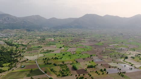 Aerial-shot-of-picturesque-plateau-with-agricultural-fields,-mountains-in-background