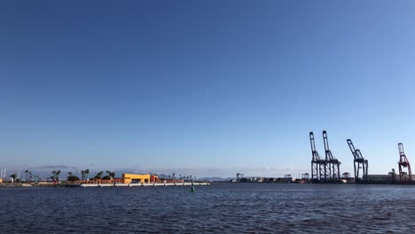 Zeitlupenclip-Eines-Industriedockhafens-Mit-Industriecontainern-Und-Kränen-Im-Hintergrund-Und-Einem-Wunderschönen-Blauen-Himmel-Mit-Einigen-Möwen-Und-Dem-Meer-Mit-Wellen