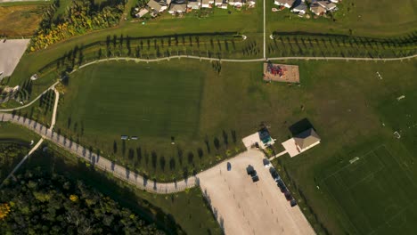 Top-down-dolly-right-4k-shot-of-a-beautiful-lush-green-soccer-park-with-walking-paths-and-play-structures-nearby