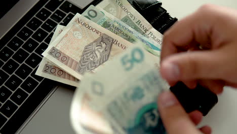 Cuente-El-Dinero-Y-Póngalo-En-Una-Billetera-Negra-Sobre-Una-Laptop,-Moneda-Nacional-Polaca,-Billete-De-Dinero-En-Zloty-Polaco