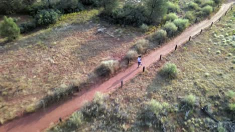 Woman-running-on-dirt-track-through-Sedona-Arizona-desert,-aerial-tracking-view